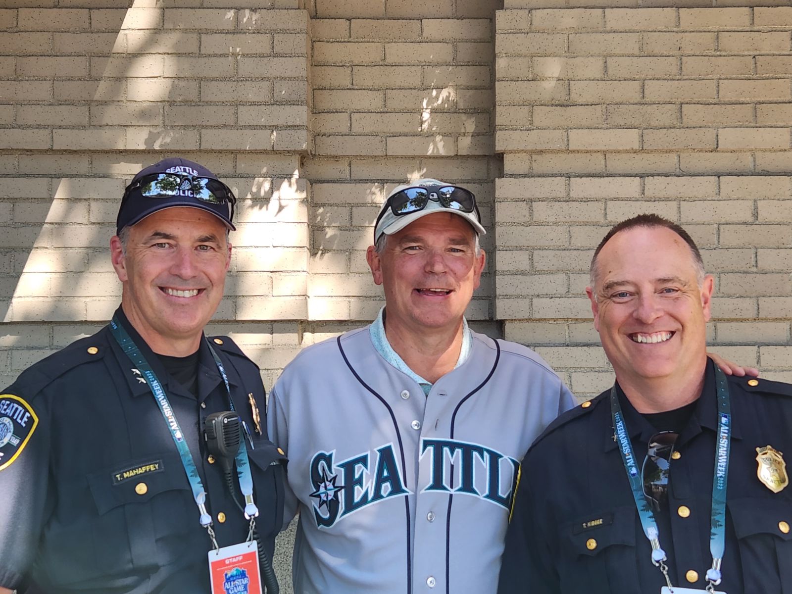 Seattle Police officers Tom Mahaffey and Todd Kibbee flanking JJ, Jeff Johnson, in a Mariners jersey at Seattle All-Star Week, 2023